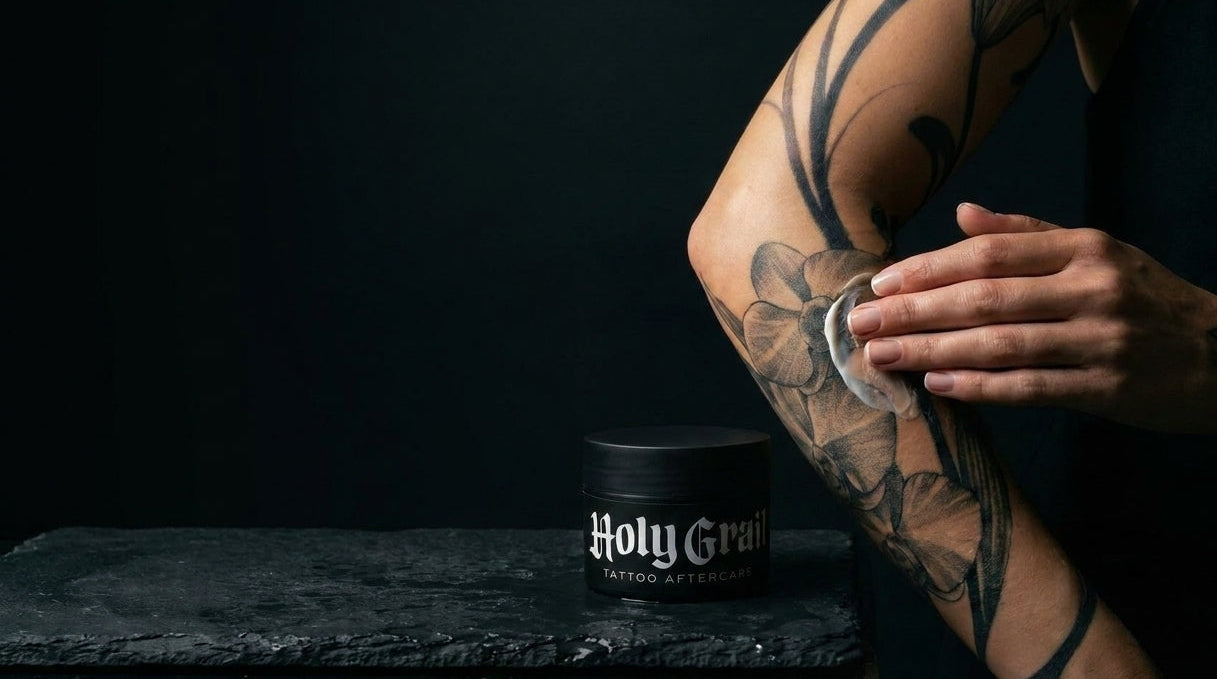 Person with tattoos holding a 'Holy Grail' after-shave product against a dark background